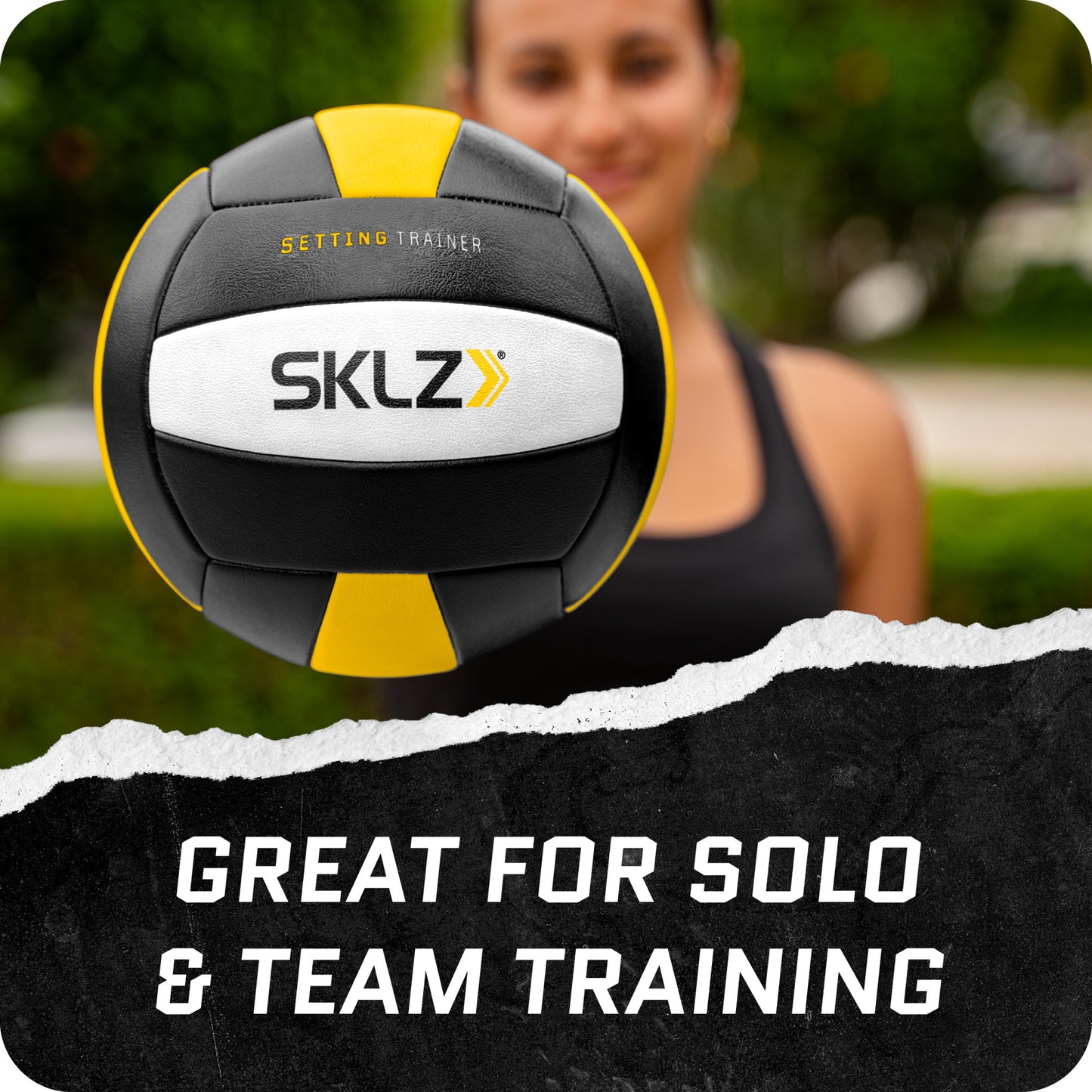 A woman holds a SKLZ training ball in front of her in an outdoor park setting