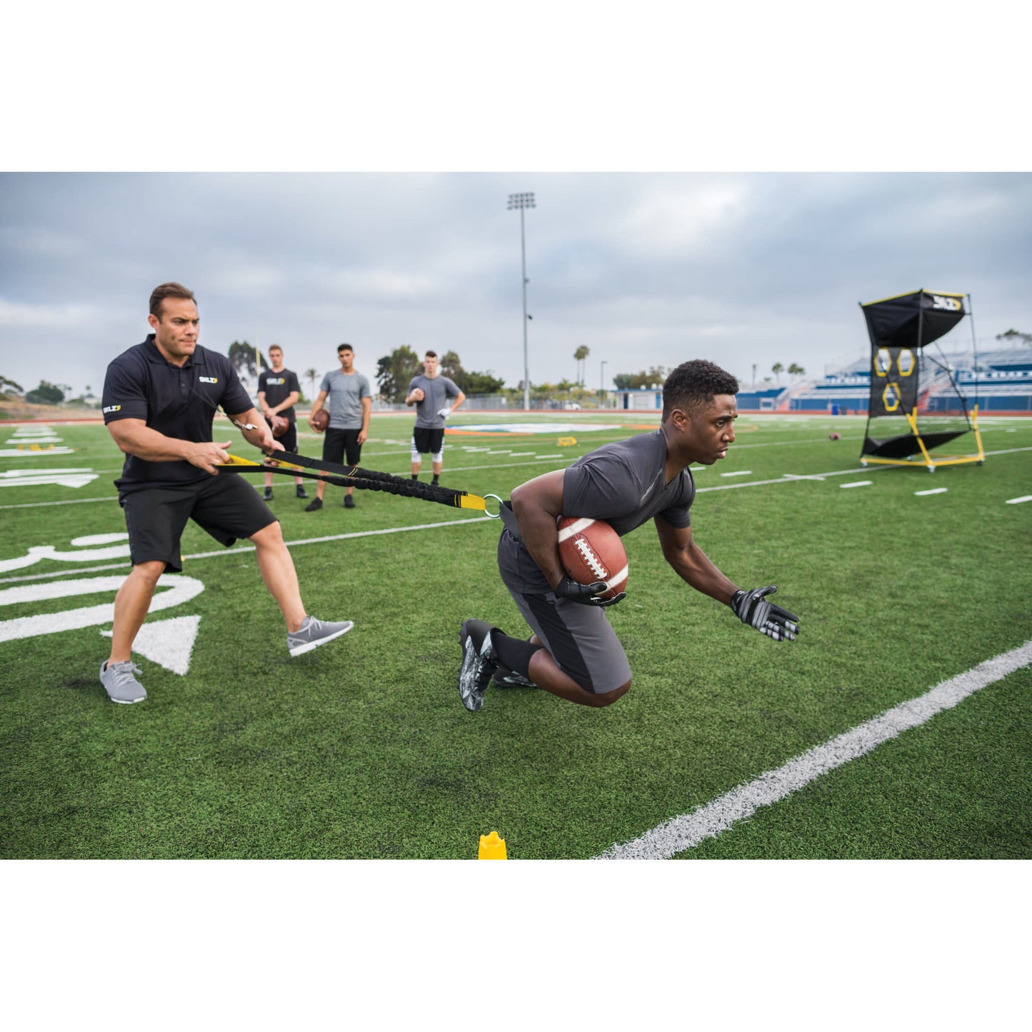 Male athlete using SKLZ Acceleration Trainer with a Coach on a football field near the end zone