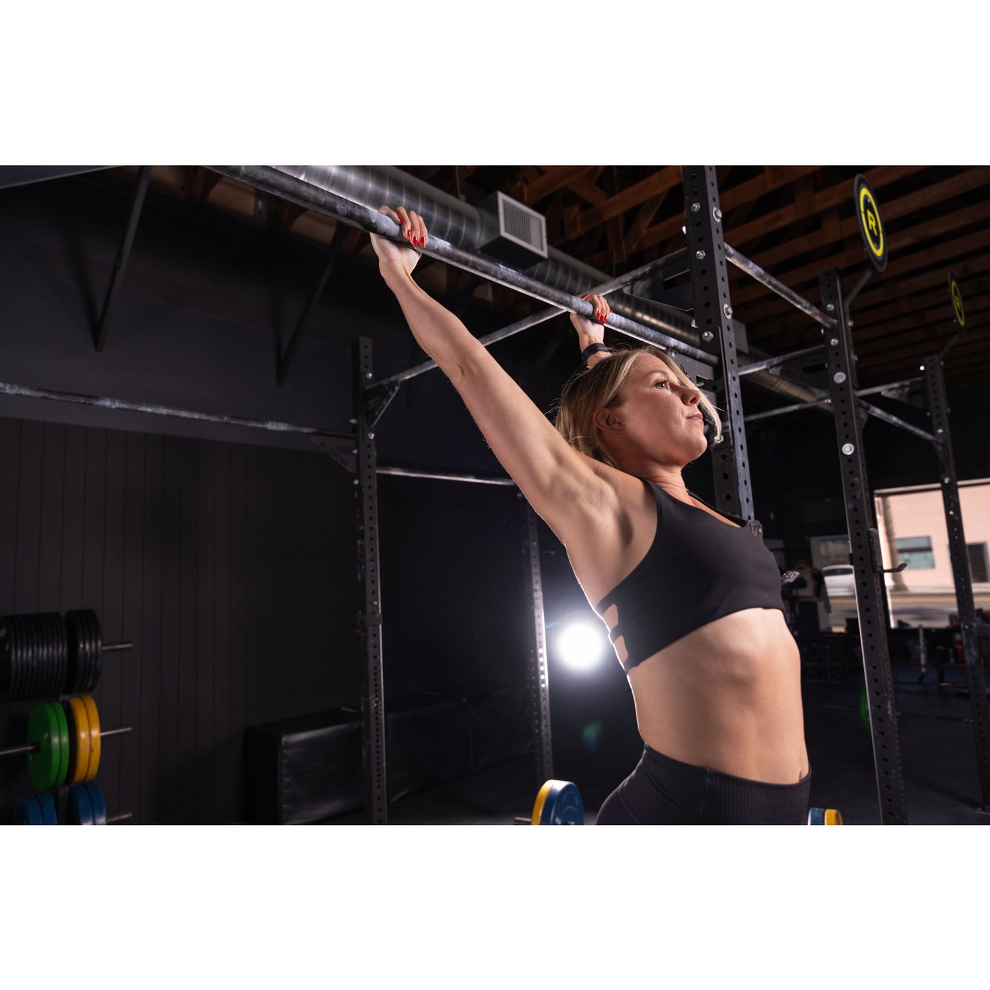 Person lifting barbell overhead in a gym, framed by metal workout equipment.