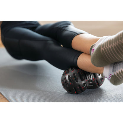 Person uses a massage ball for targeted muscle relief on a yoga mat in a home setting