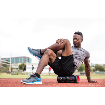 Man performs stretch exercise on field with portable speaker nearby during outdoor workout