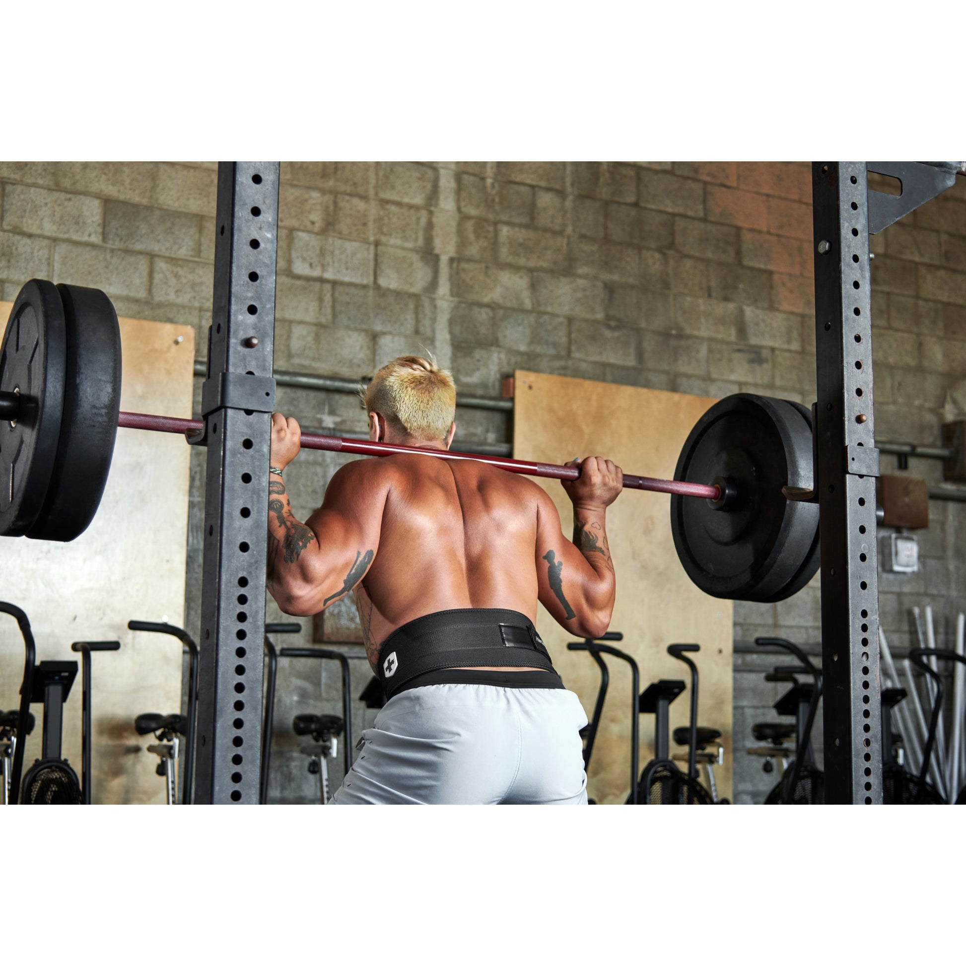 Person lifting weights on a squat rack in a gym environment.