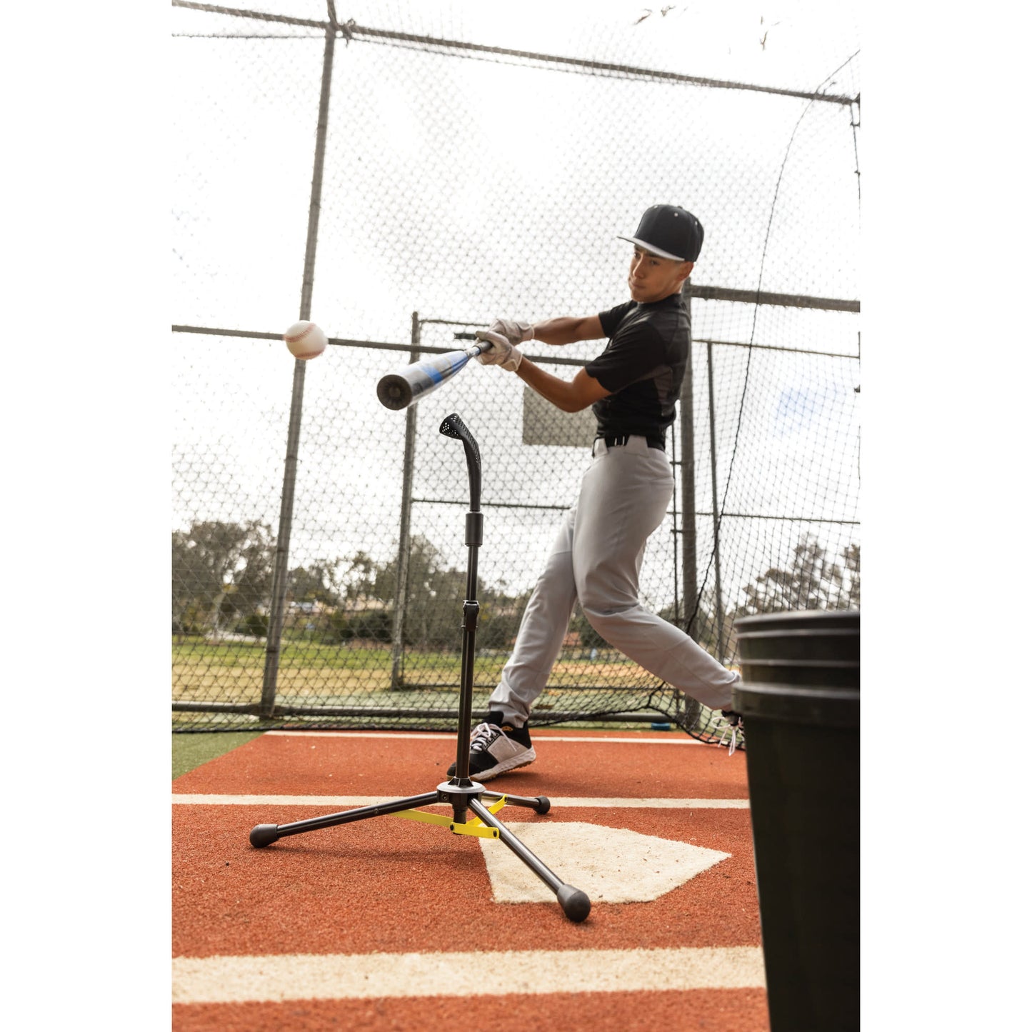 Baseball player swings at ball in batting cage during practice