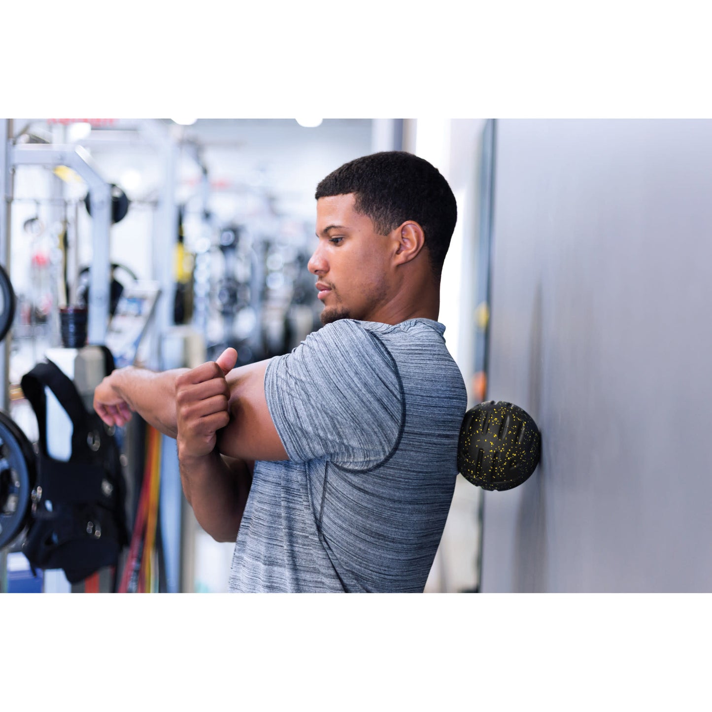 Man stretches arms with takball against gym wall in fitness center setting