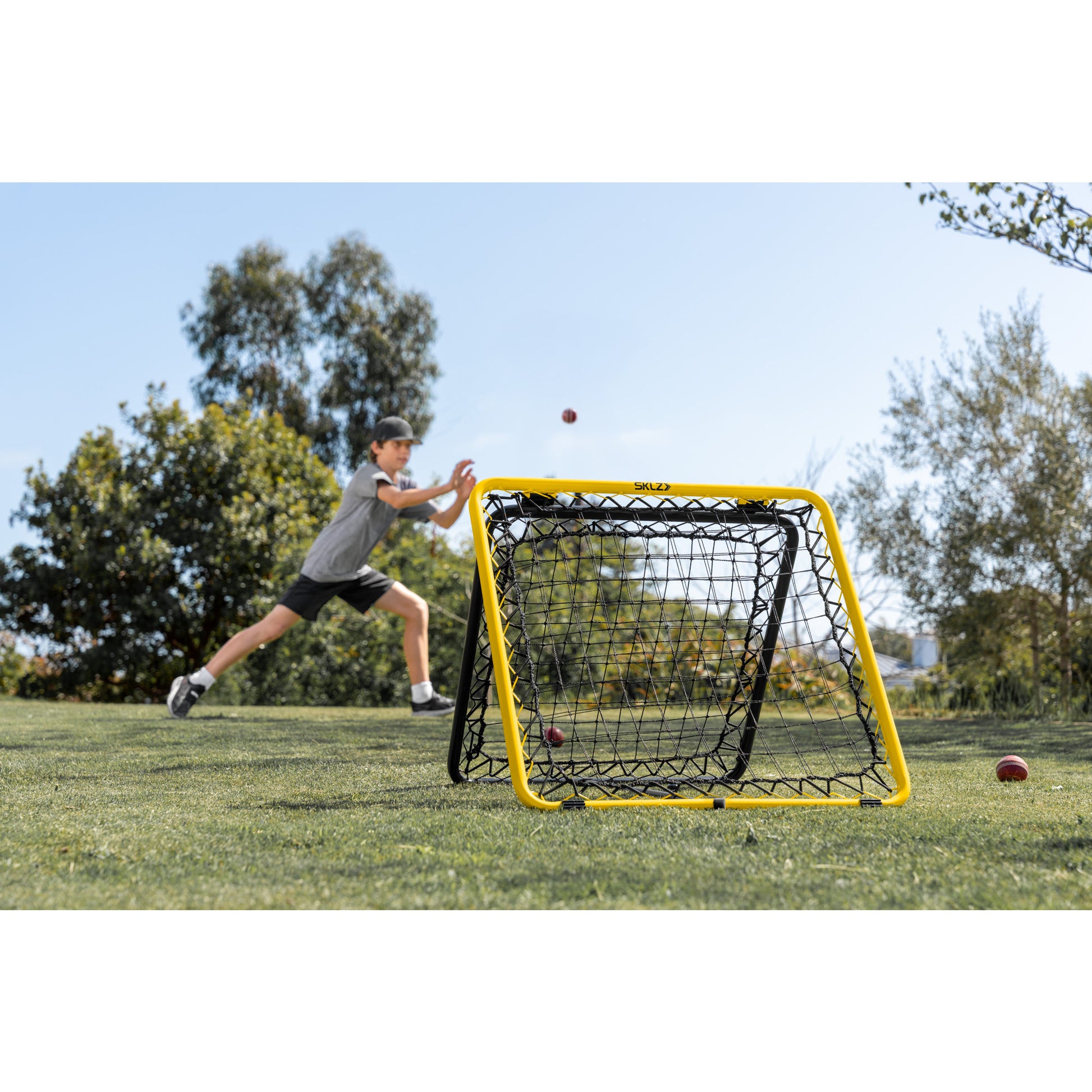 A child throws a baseball towards a portable target on a grassy field outdoors.
