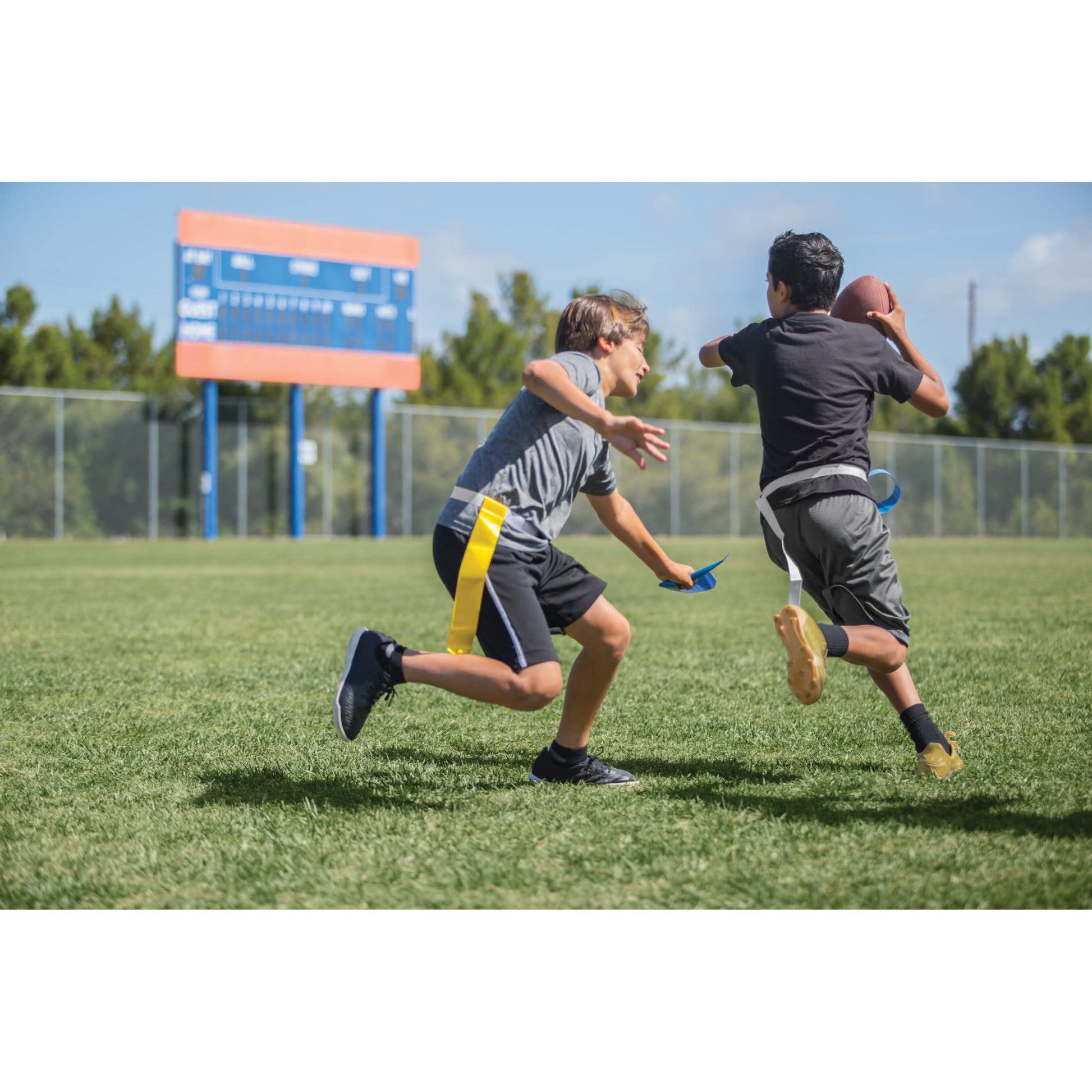 Two boys run and chase a football on a grassy field during daytime.