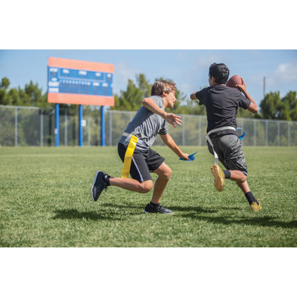 Two boys run and chase a football on a grassy field during daytime.