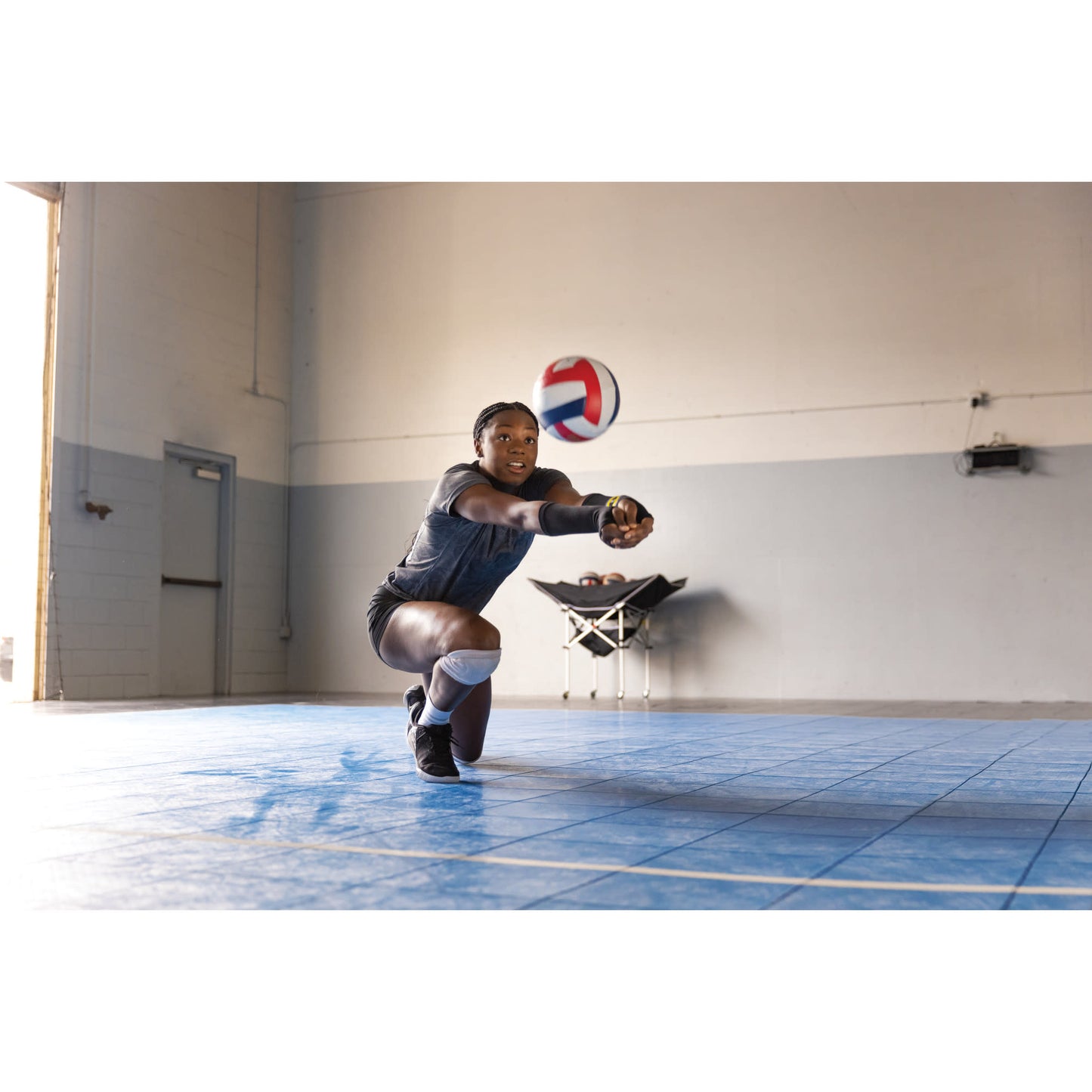 A girl dives to hit a volleyball on an indoor court in a gymnasium environment
