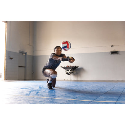 A girl dives to hit a volleyball on an indoor court in a gymnasium environment
