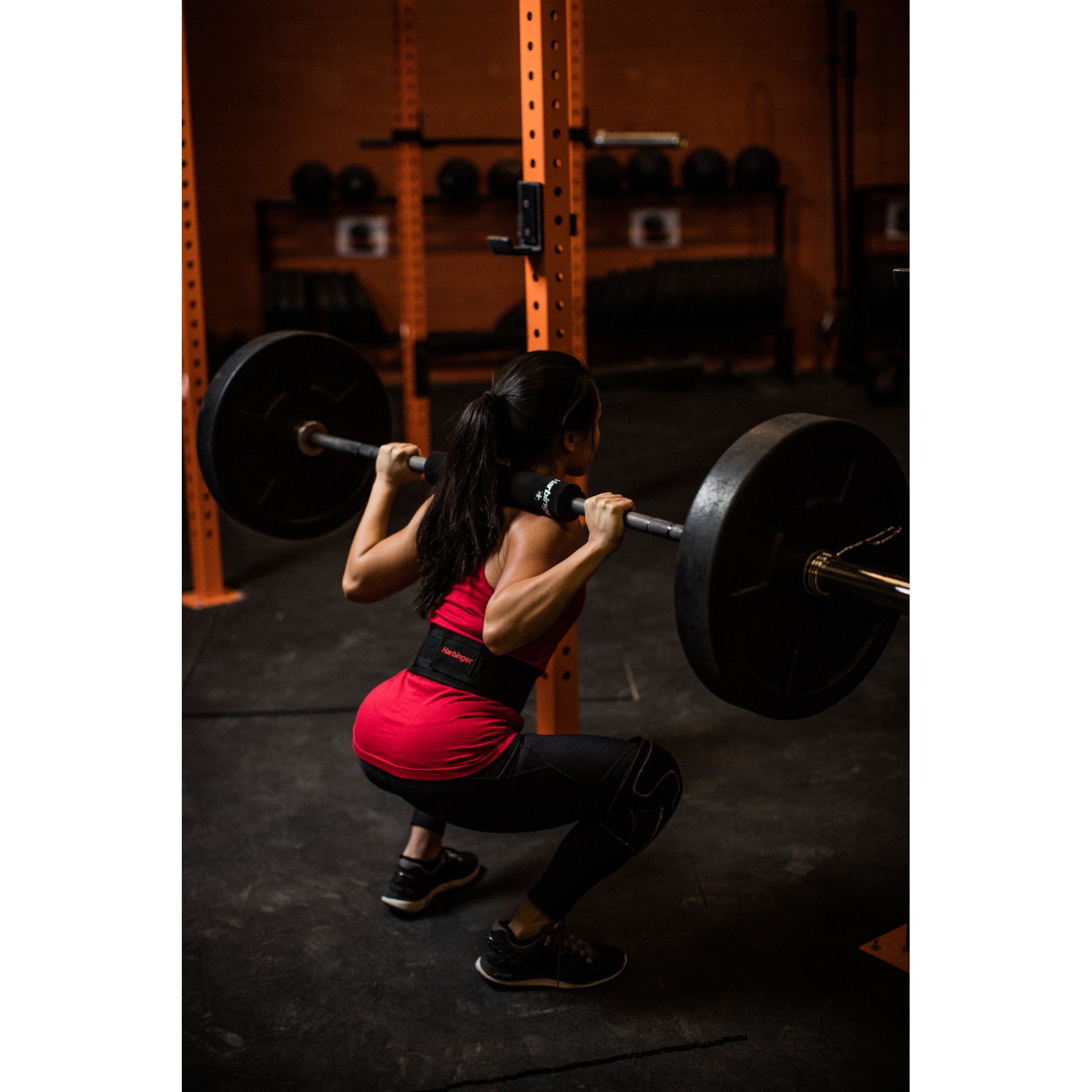 Person squats with barbell in gym, surrounded by weights and equipment.