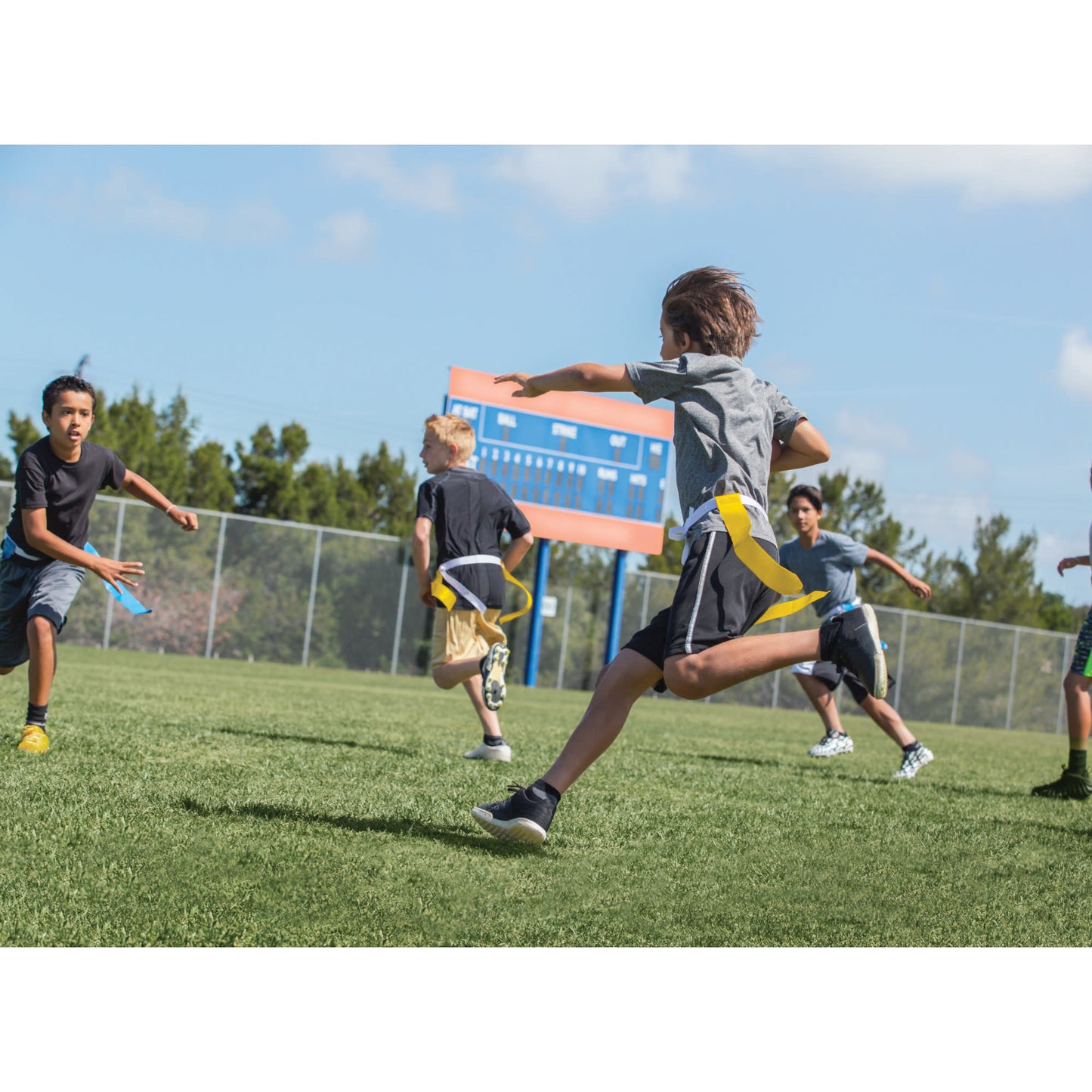 Children run and play flag football on a grassy field outdoors