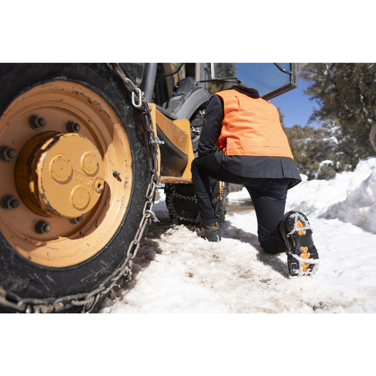 A person kneels beside a tracked vehicle outdoors in snow during daytime