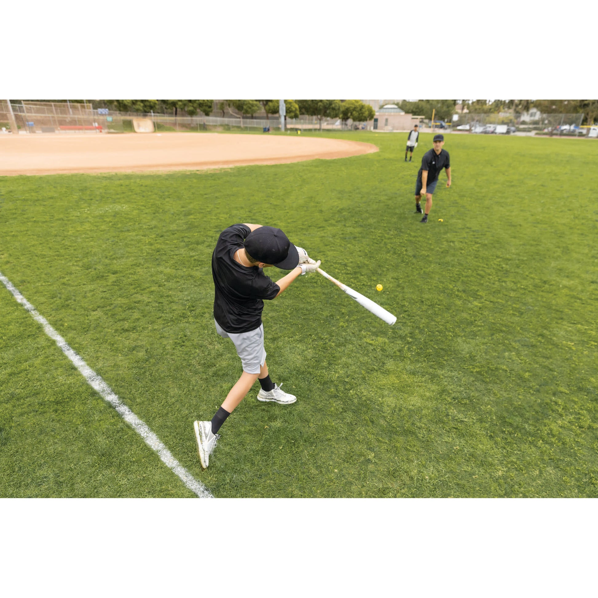 Boy swings a bat at a baseball on a grassy field during practice