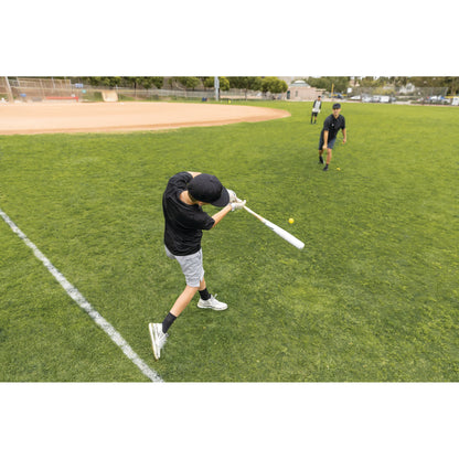 Boy swings a bat at a baseball on a grassy field during practice