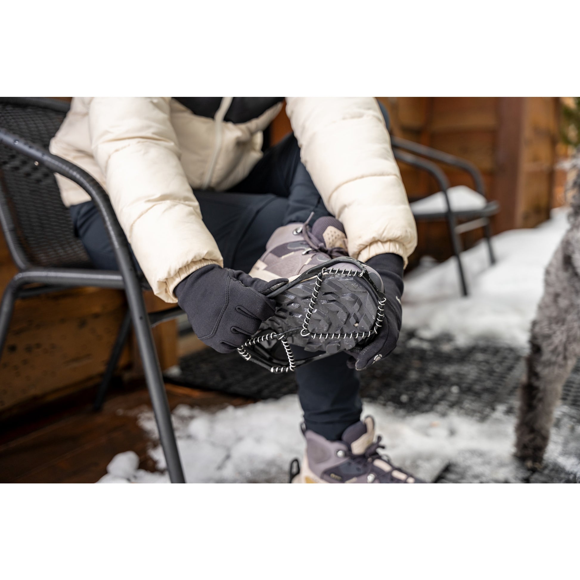 Person wearing gloves and snow boots checks a device while sitting outside near snow and wooden structure