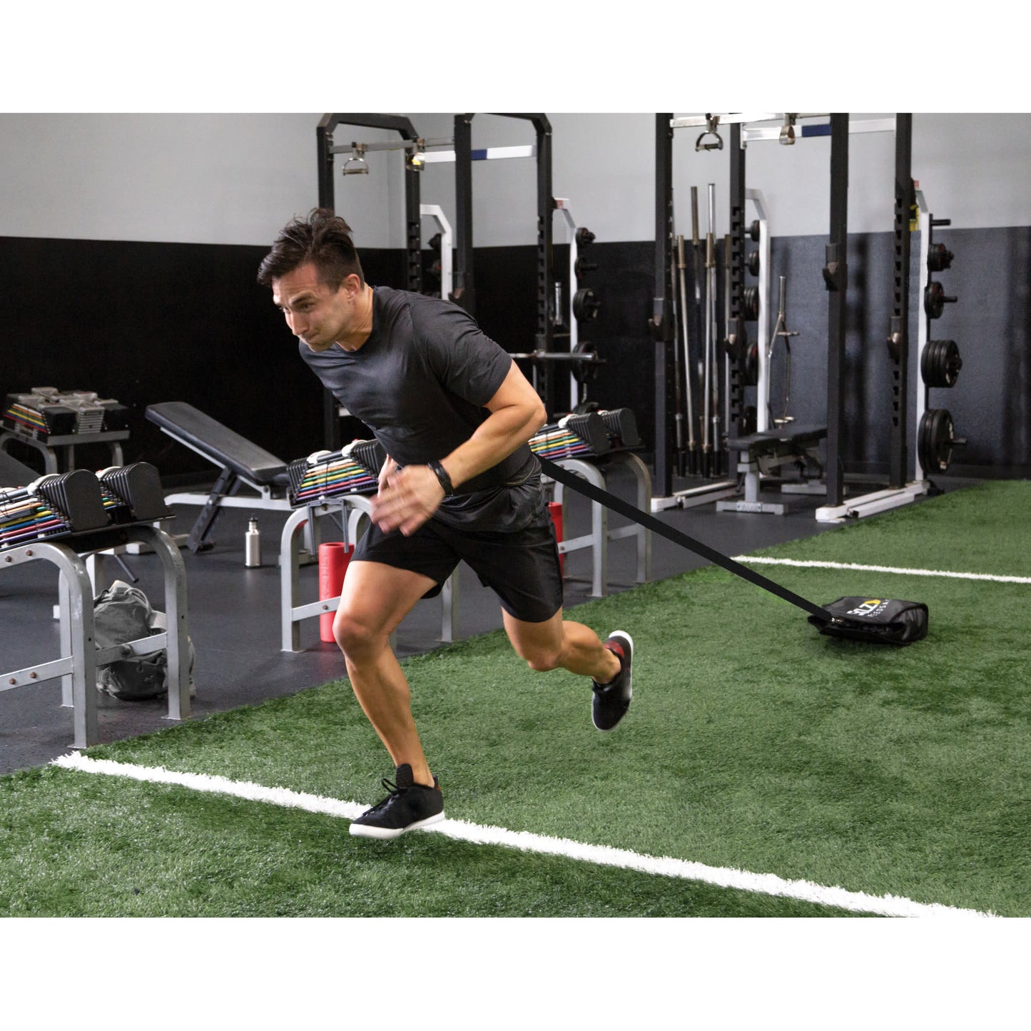 Man runs on turf pulling sled for resistance training in gym with weight equipment