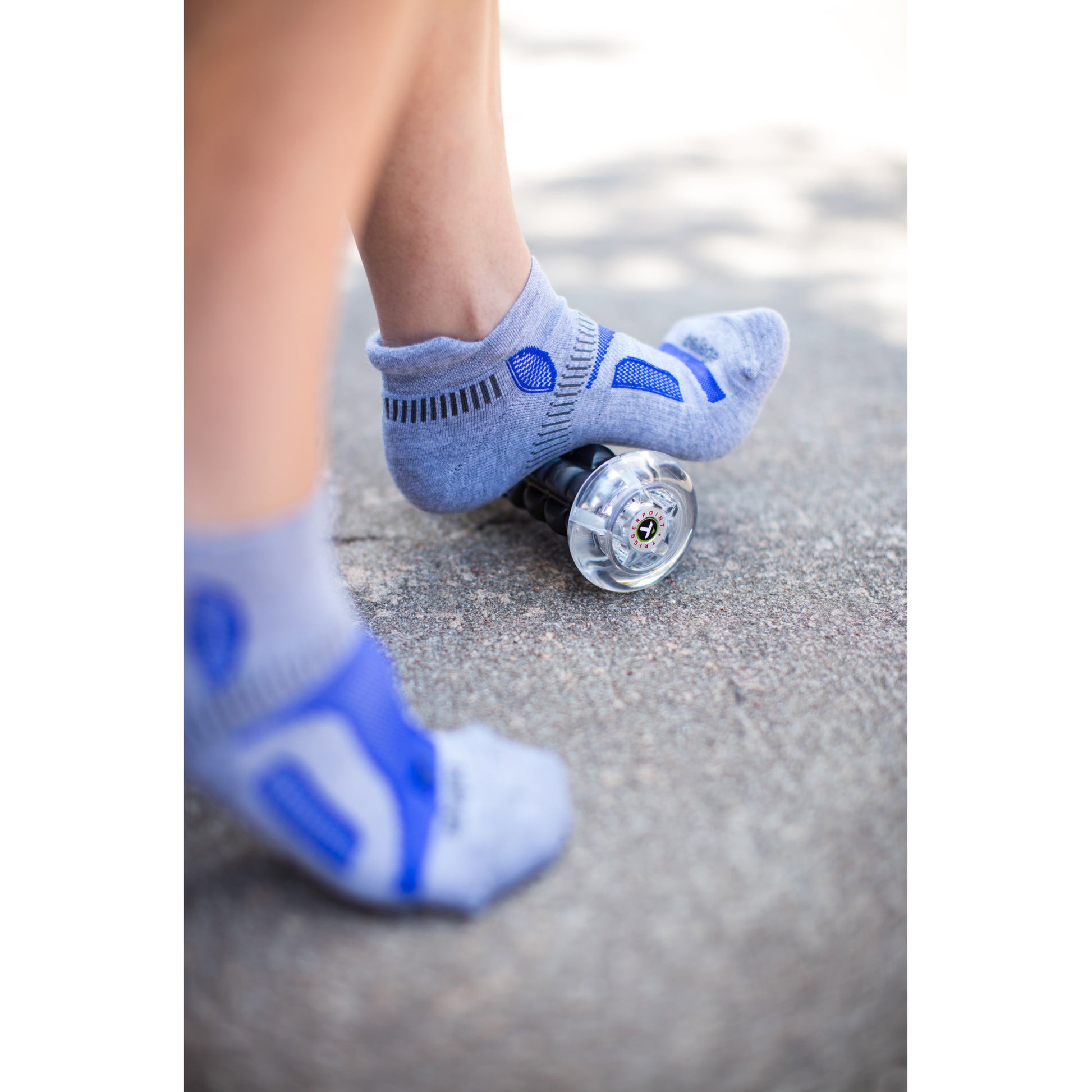 A child's foot in a sock balances on a skateboard on pavement in an outdoor setting