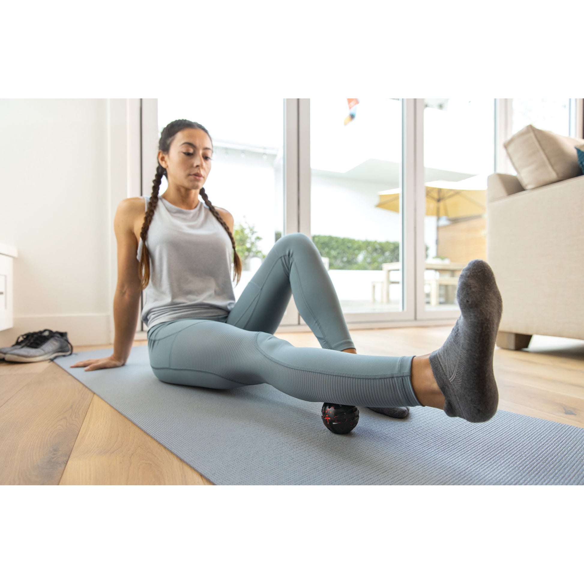 Woman uses foam roller on leg during indoor workout on yoga mat in home.