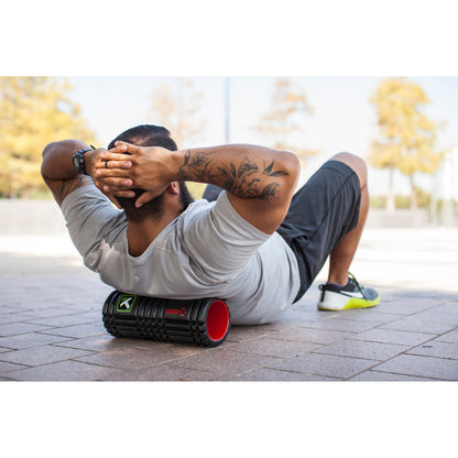 Man performs abdominal exercise on an outdoor pavement with a portable foam roller.