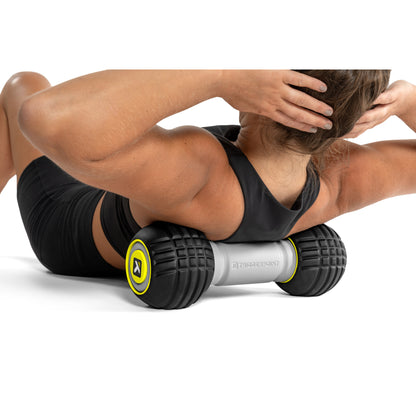 A person uses a foam roller to massage their back while lying on the floor in a workout environment.