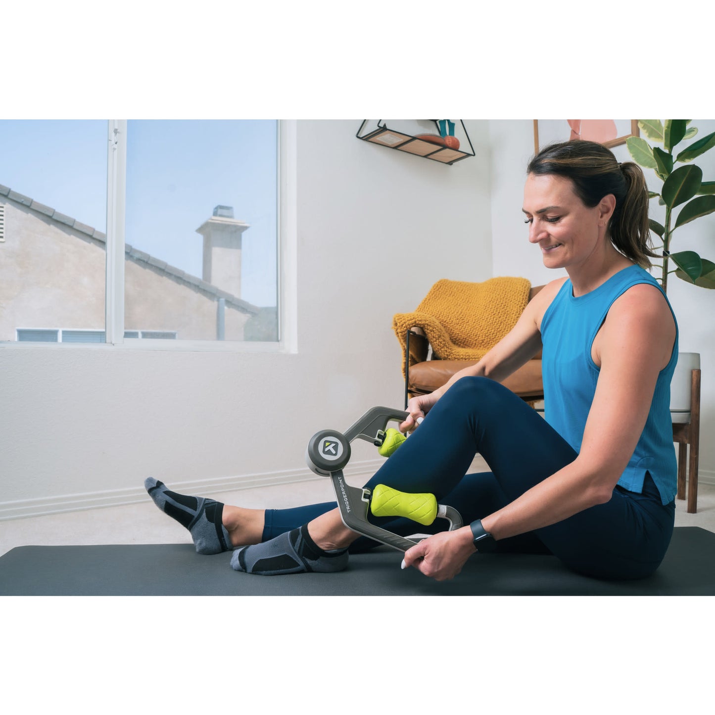 Woman exercises with a fitness device indoors near a window in living room.