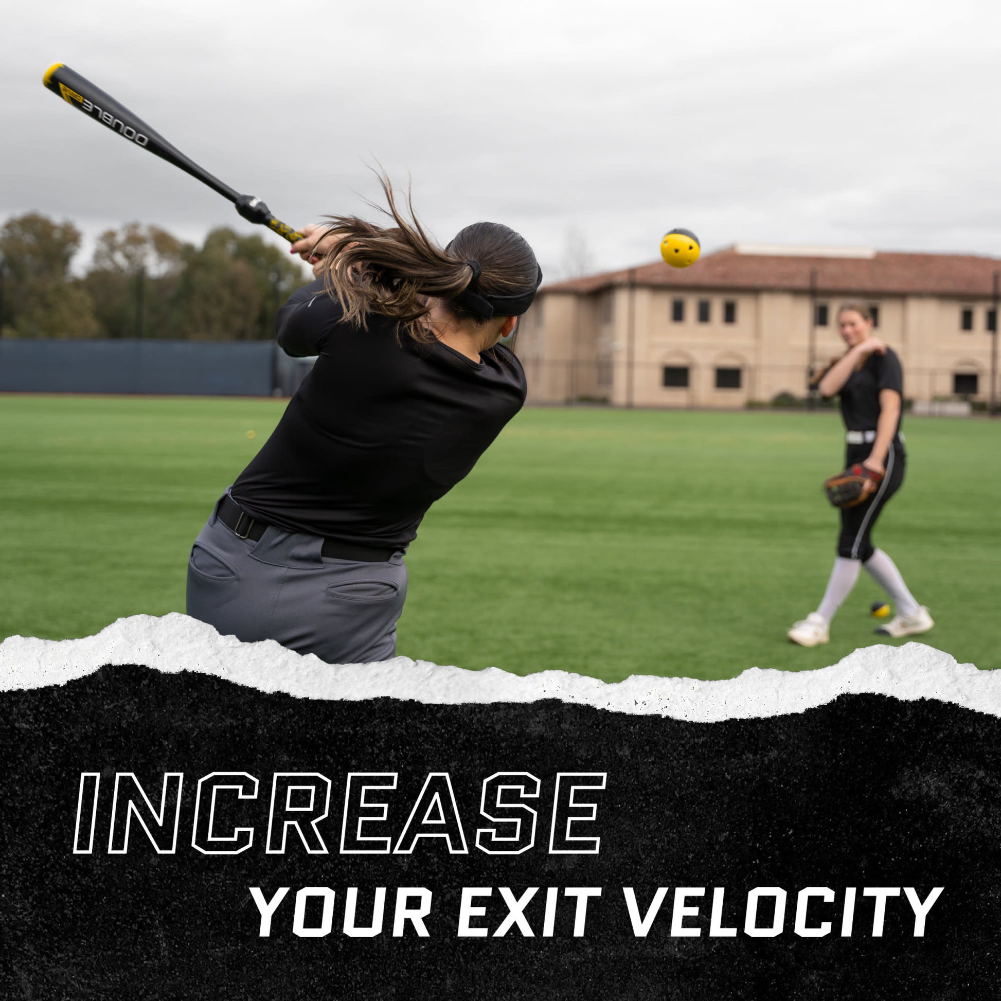 Woman swings a baseball bat on a field while another stands ready with a glove in the background