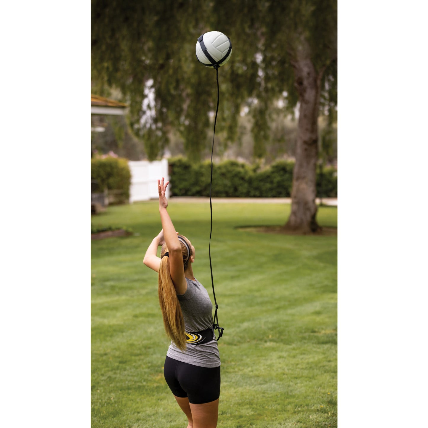 A woman drops a volleyball while wearing headphones in a grassy park area