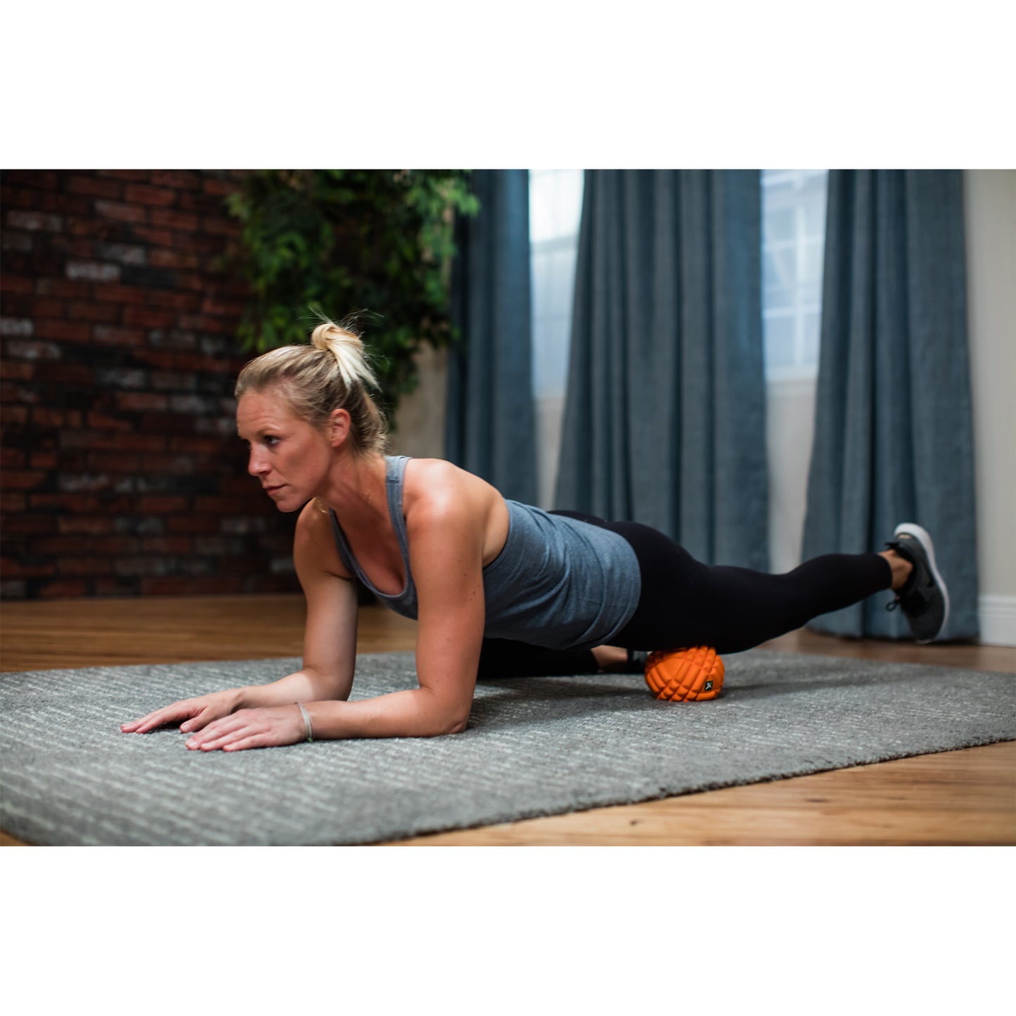 Woman exercises with a foam roller on carpet indoors at home.
