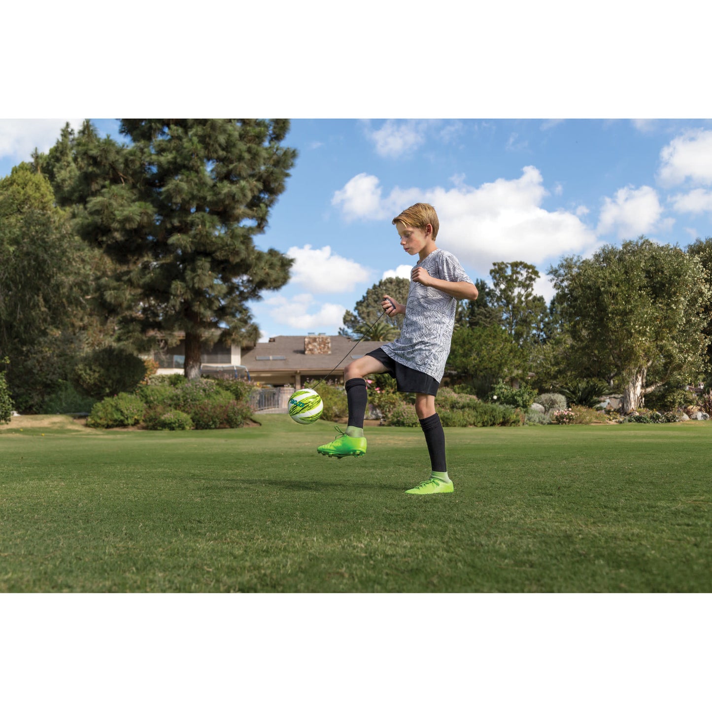 Boy kicks soccer ball on grass field in park under blue sky