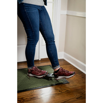 Shoes stand with ice cleats on green mat, on wooden floor near white wall.