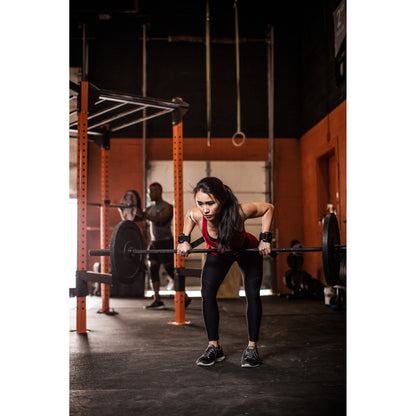Woman lifting barbell in gym while two people stand in the background.