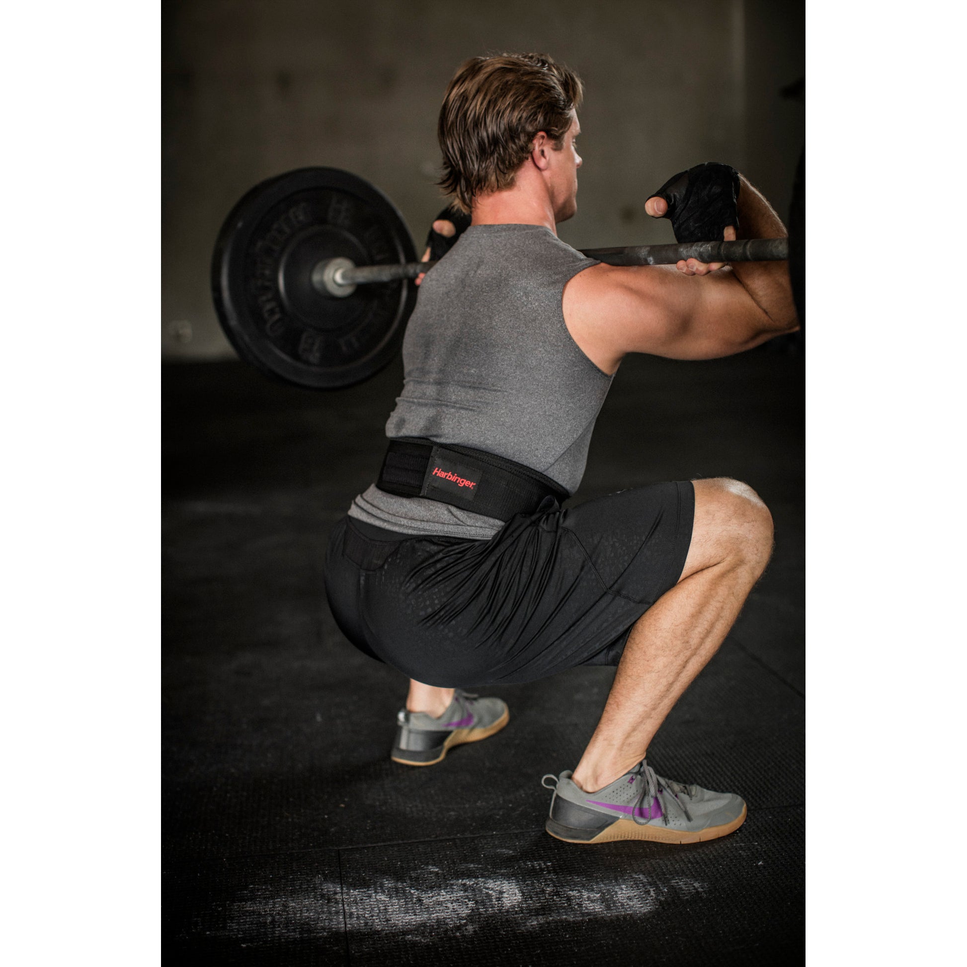 Person squats lifting a barbell in a dimly lit gym setting.