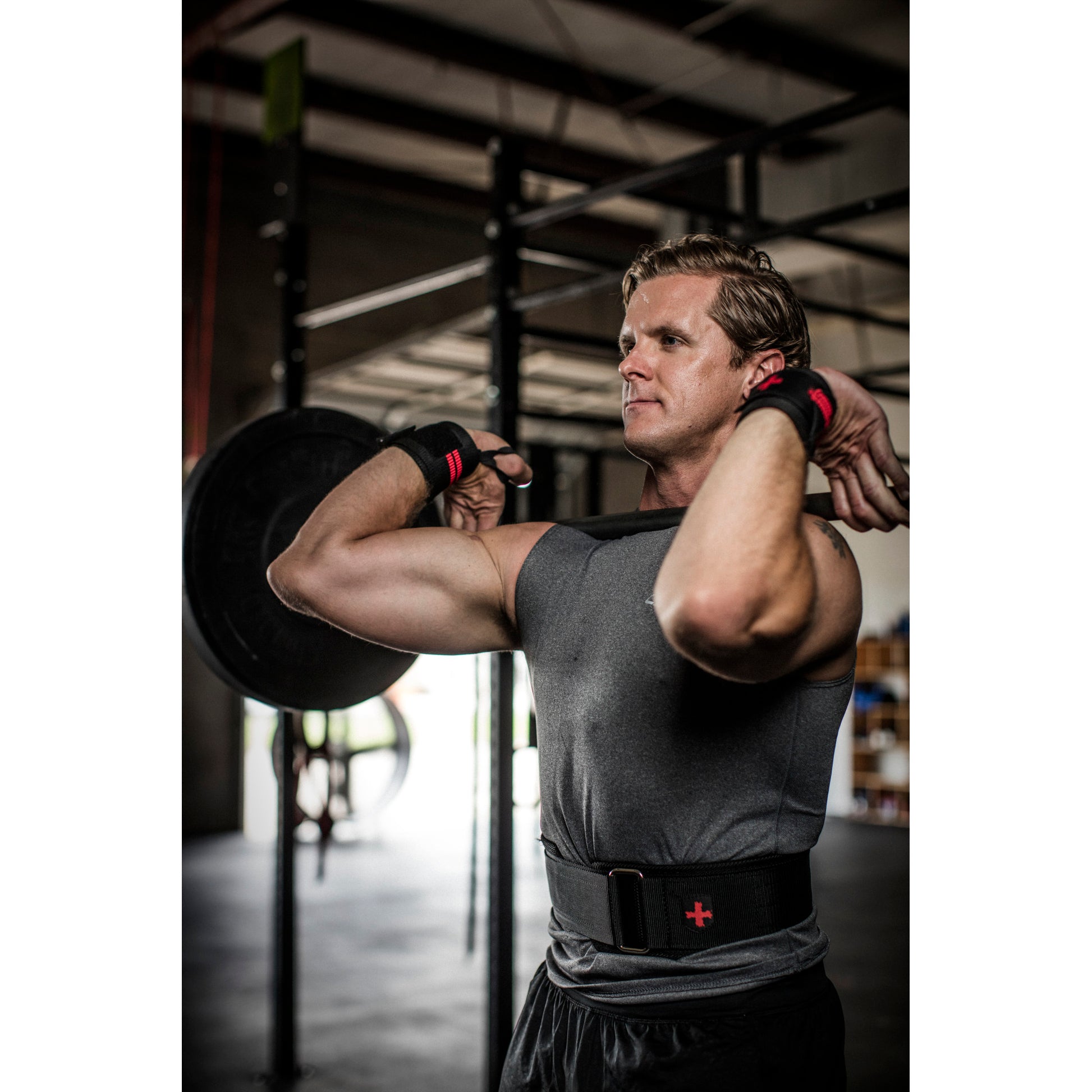Man lifting weights in a gym, wearing wristbands and a belt, focused on exercise.