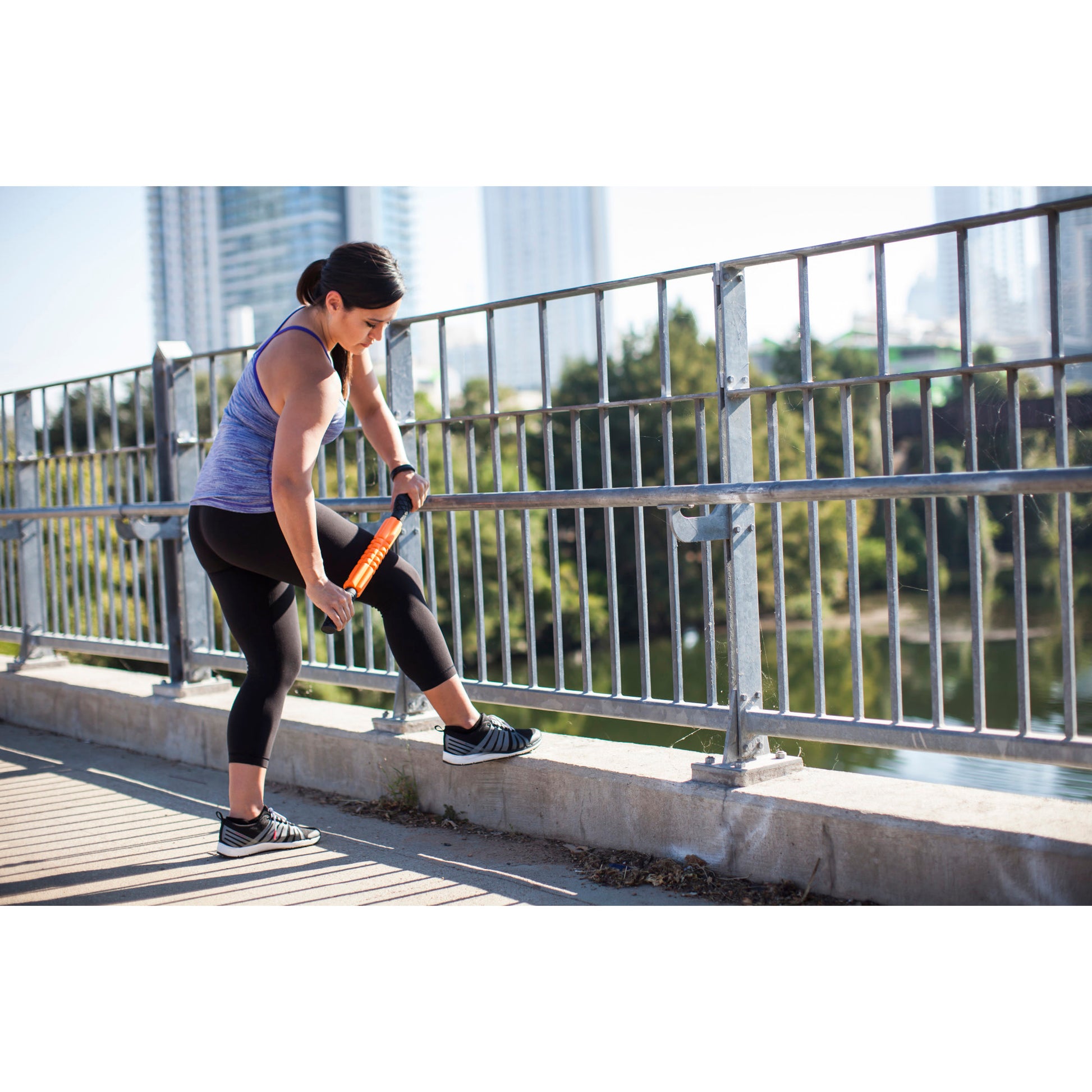 Woman stretches her leg on a railing outdoors during daytime with buildings in the background