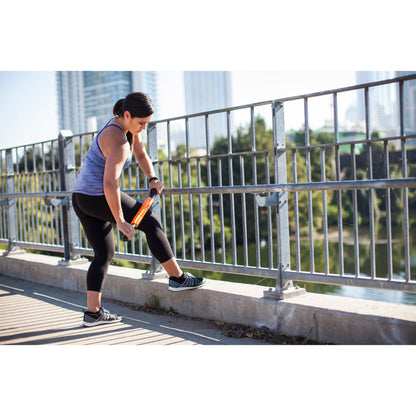 Woman stretches her leg on a railing outdoors during daytime with buildings in the background