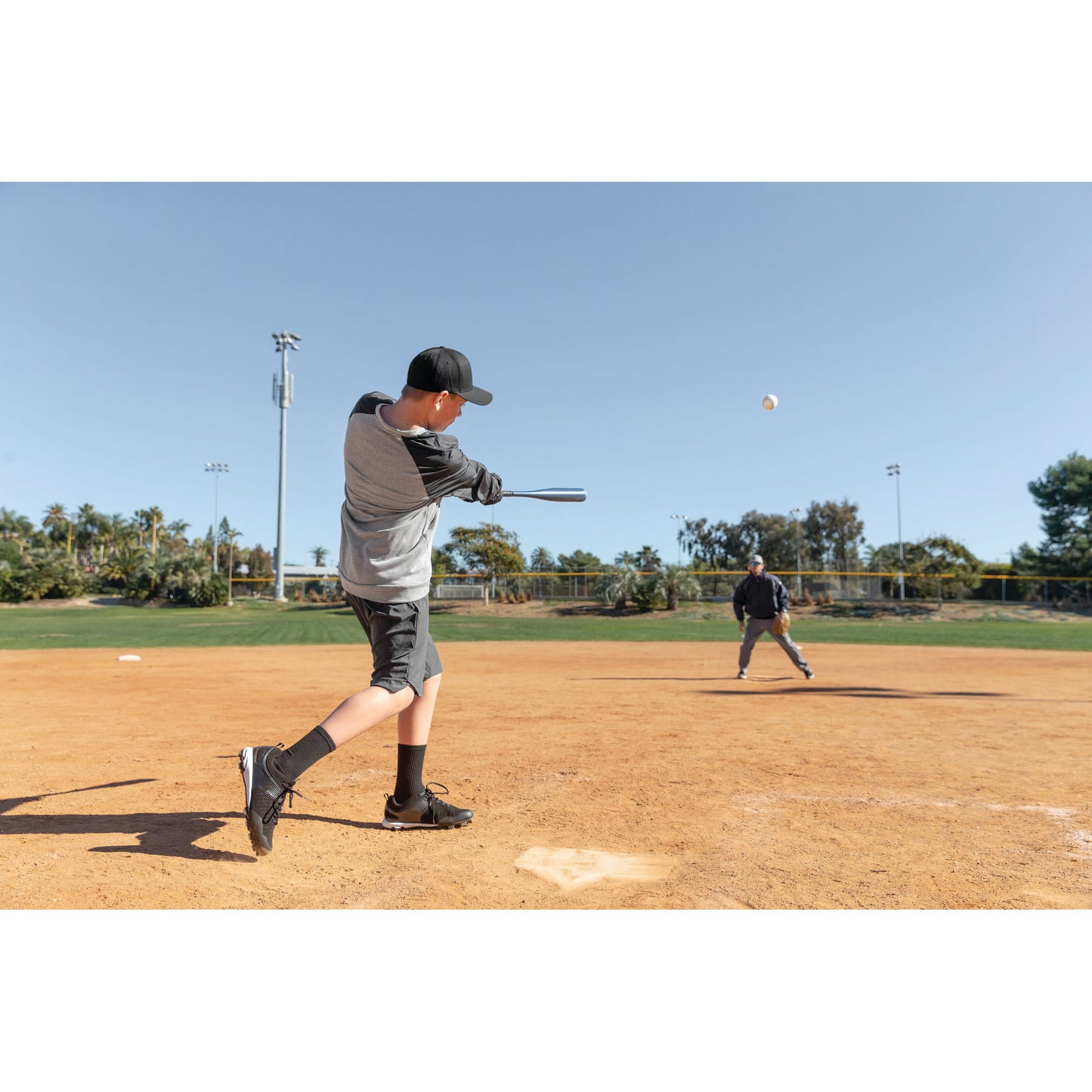 Boy swings bat at baseball on a dirt field during daytime practice