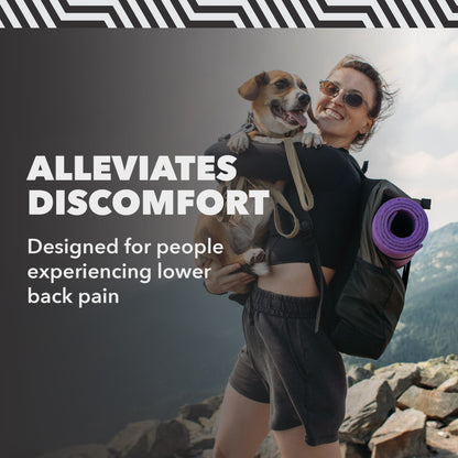 Person carries dog on mountainside, smiling and wearing backpack with yoga mat.
