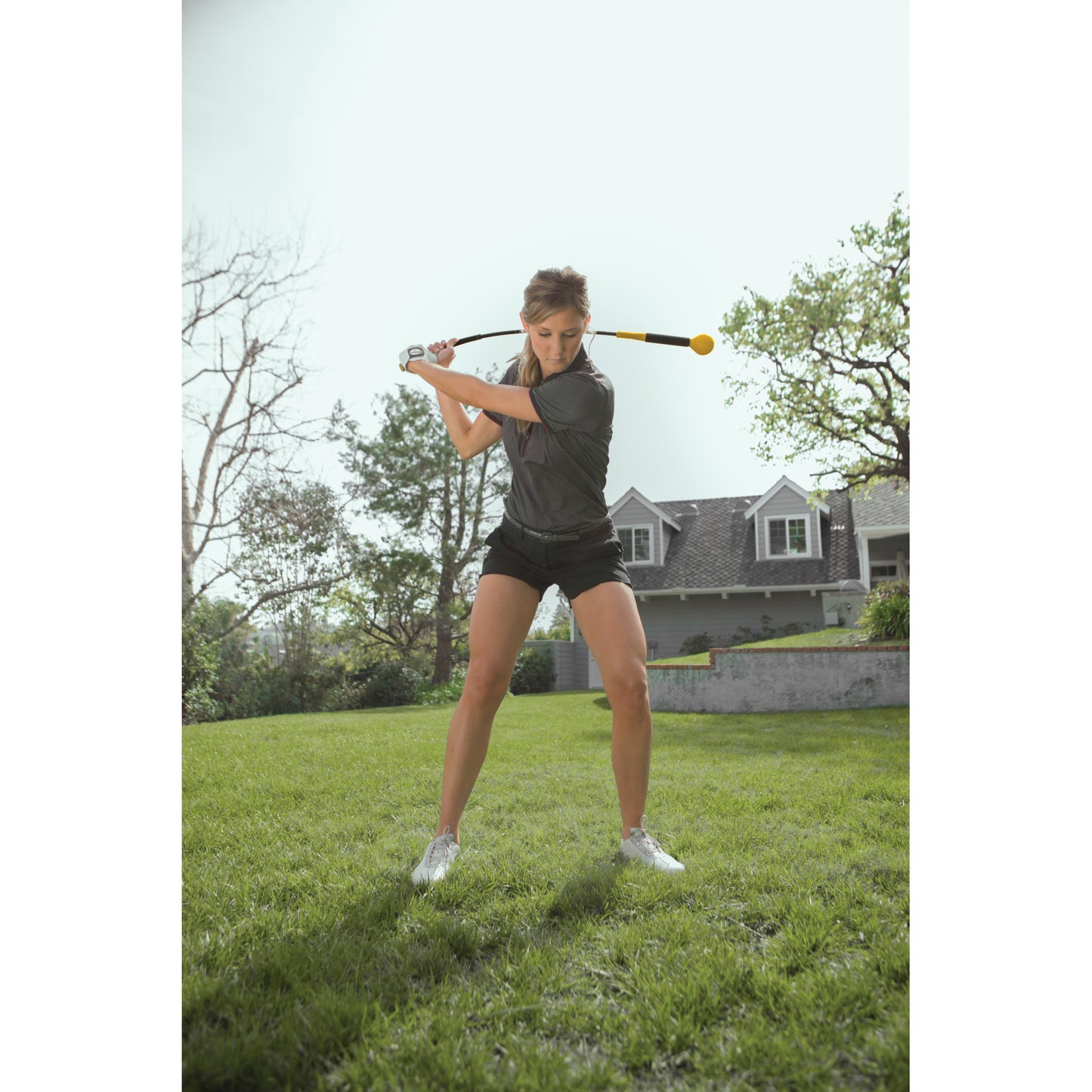 Young woman swings golf club on green lawn in front of house during daytime