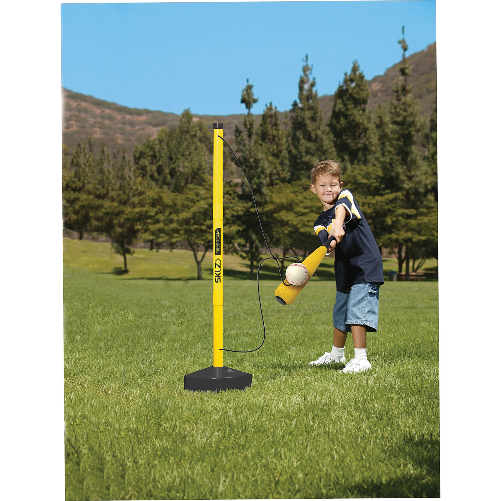 Young boy swings at a baseball attached to a pole with a bat outdoors in a grassy field