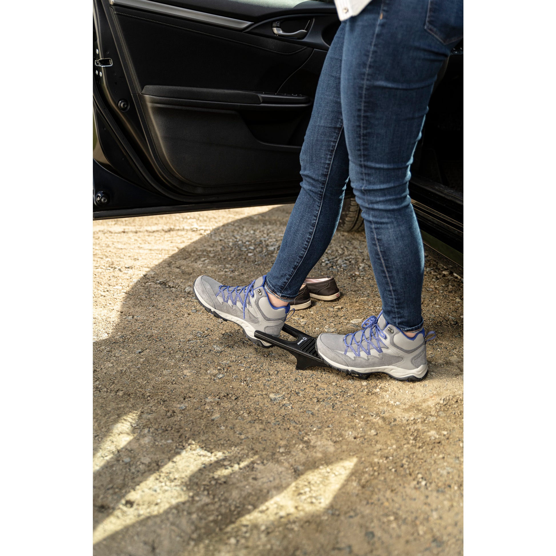 Feet step onto a car door latch hook, gravel ground, open car door.
