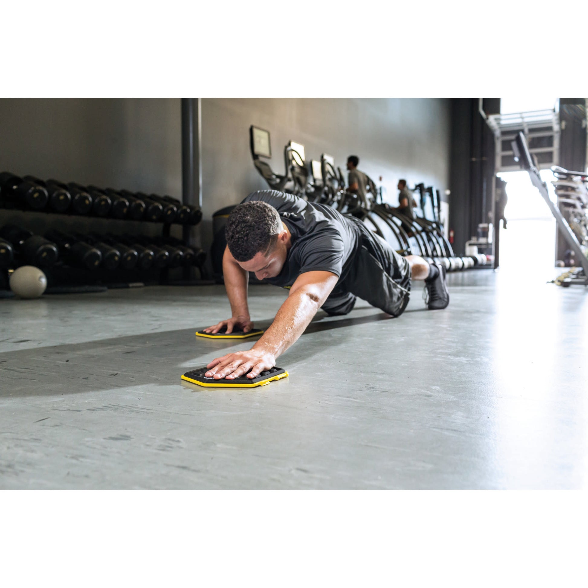 Man performs pushups with sliders on gym floor in a fitness center