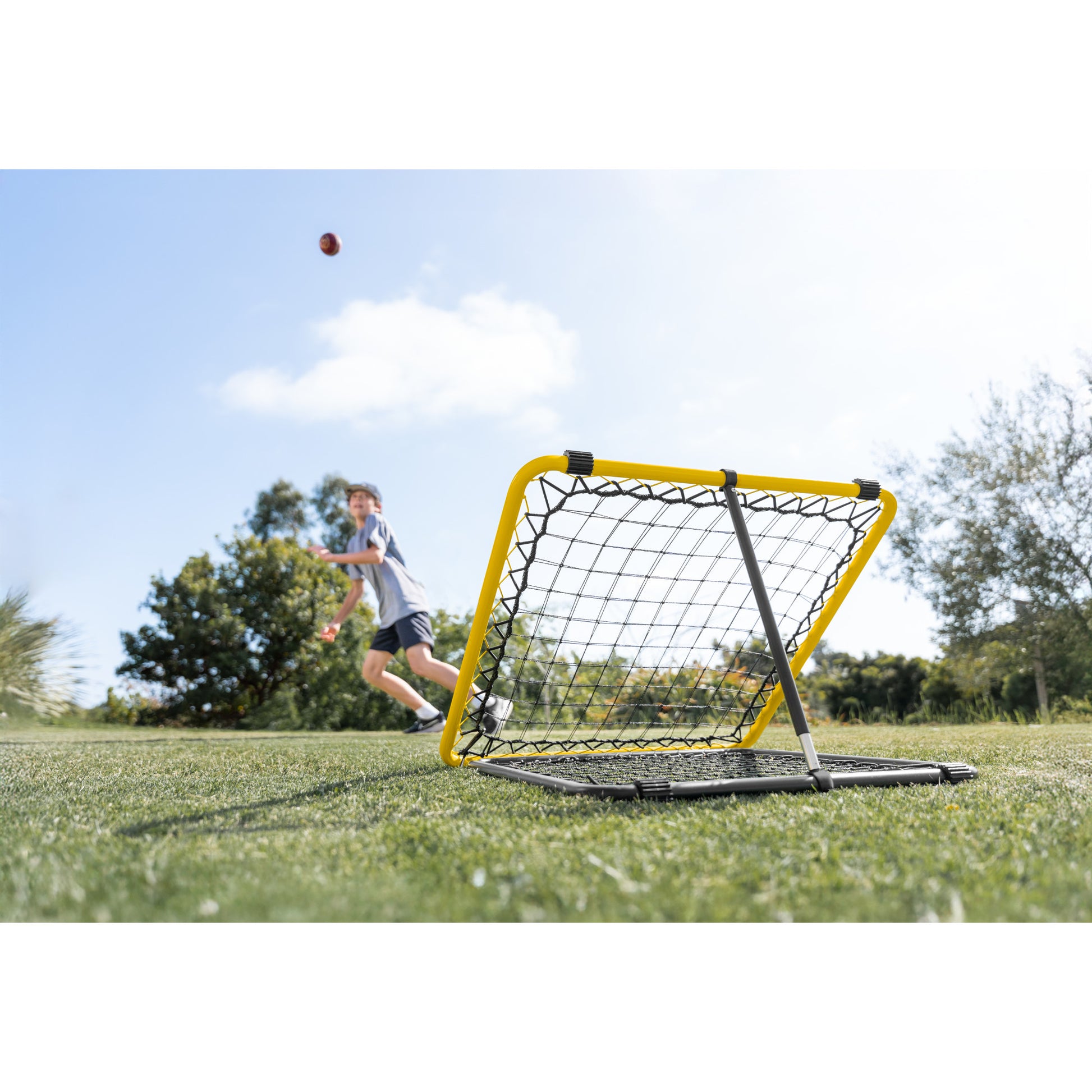 The soccer goal is set up on grass as a boy throws a ball in an outdoor field