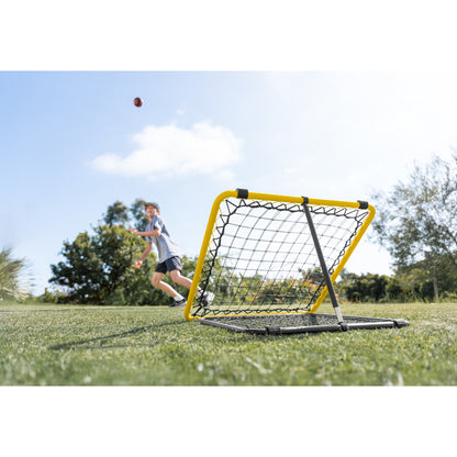 The soccer goal is set up on grass as a boy throws a ball in an outdoor field