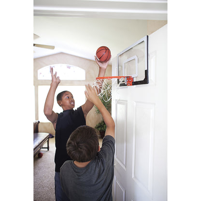 Two boys play basketball indoors near a wallmounted hoop during daytime