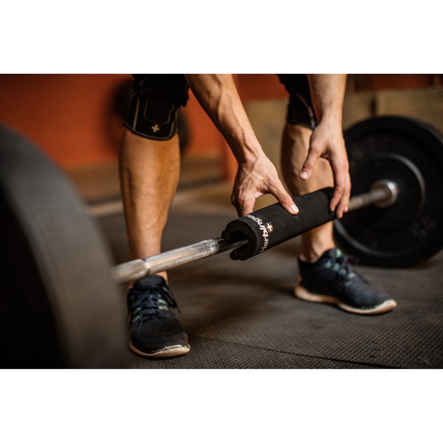 Hands grip weighted barbell on gym floor.
