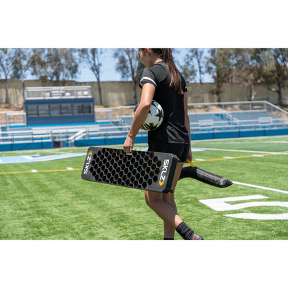 Female athlete carries soccer ball and training equipment on a football field during practice