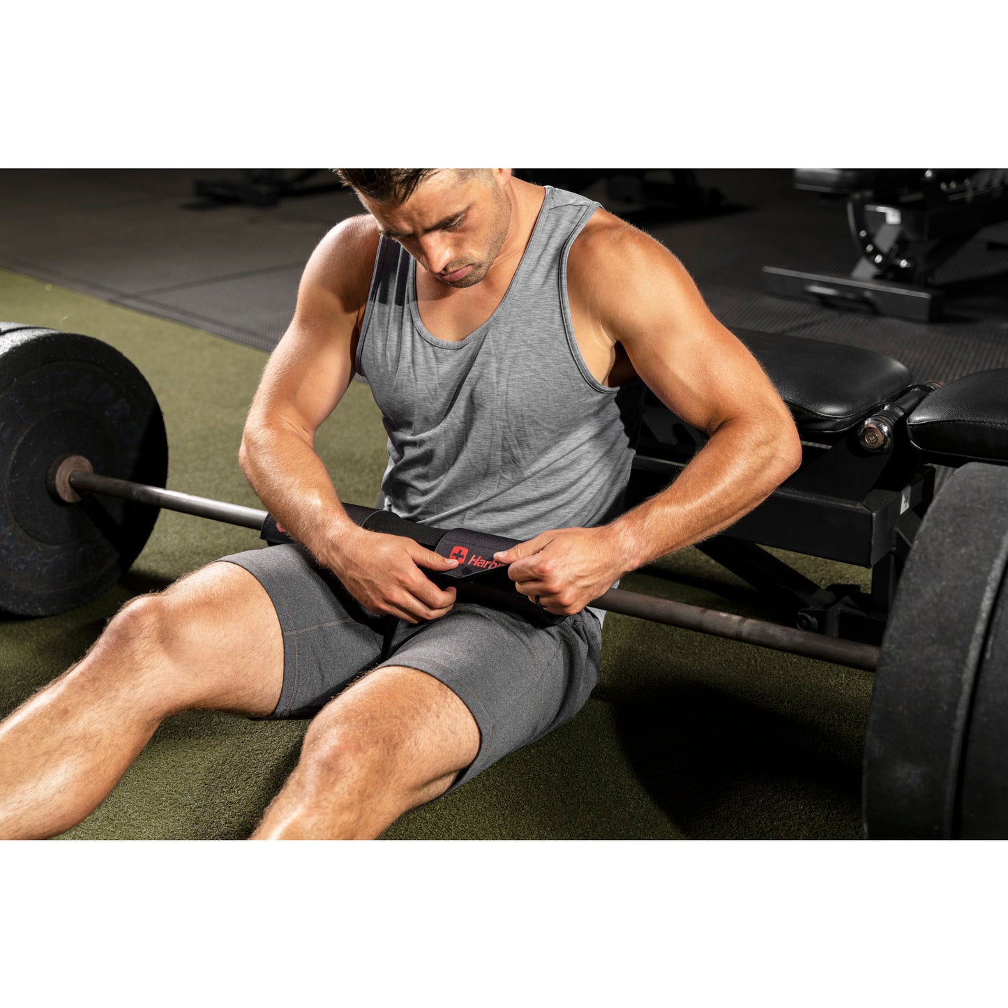 Man sits adjusting weightlifting belt, resting near barbell in gym.