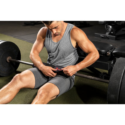 Man sits adjusting weightlifting belt, resting near barbell in gym.