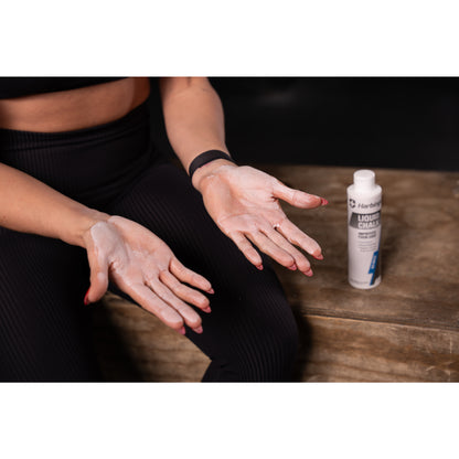 Hands apply liquid chalk indoors, seated near a wooden surface.