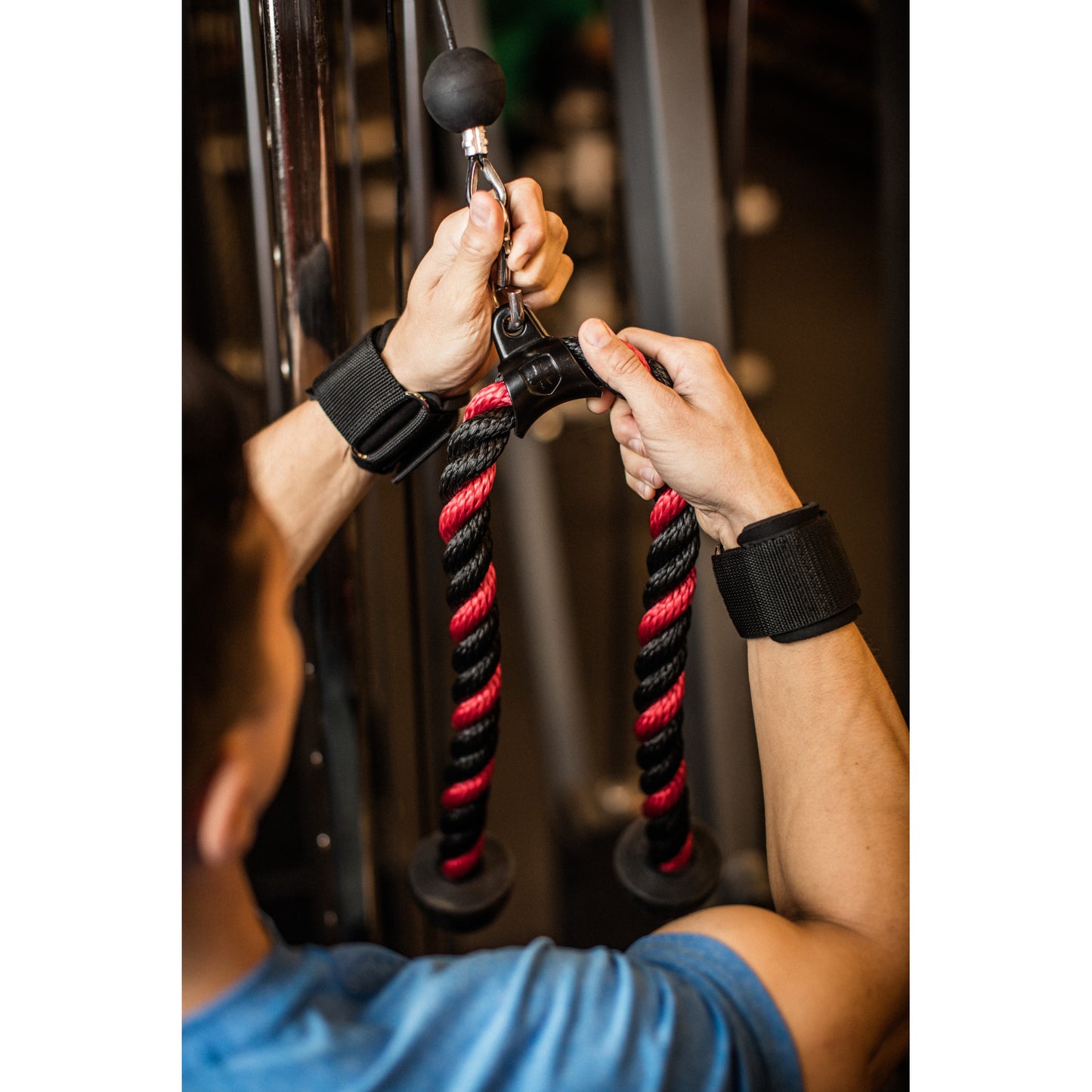 Hands grip gym cable rope in workout area.